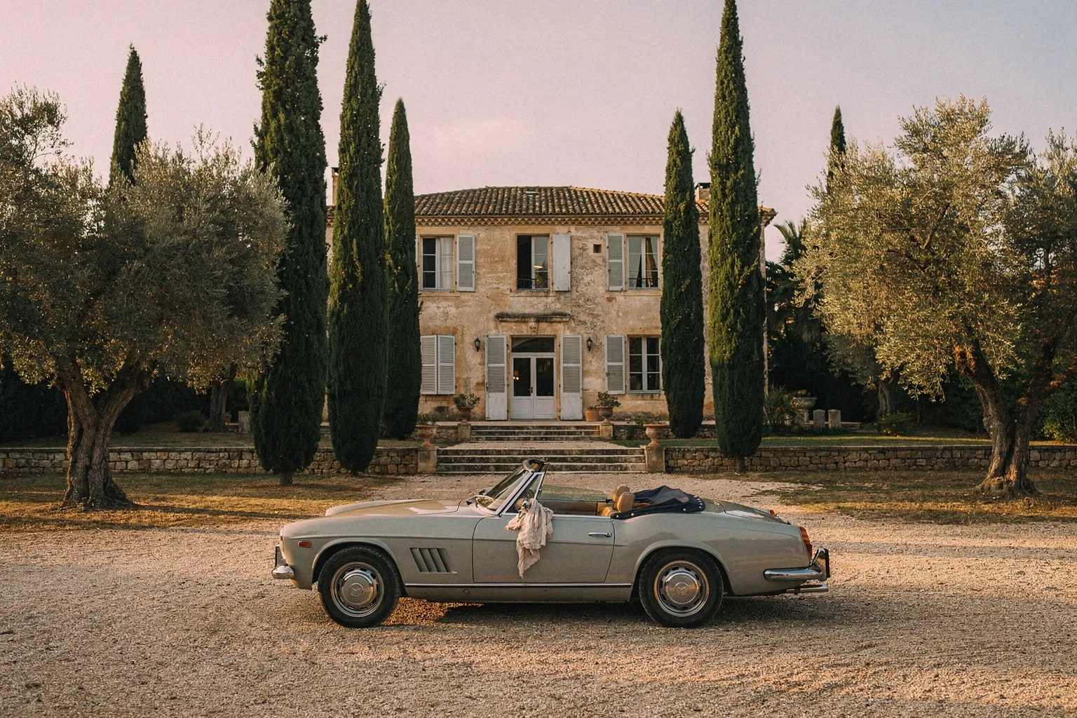 A vintage touring car approaching a private stone estate in Provence at sunrise